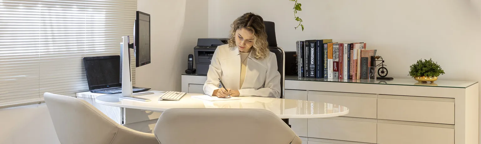 Dra. Daiane Saldanha no consultório, escrevendo à mesa